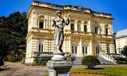 Statue of woman on pedestal in front of mansion