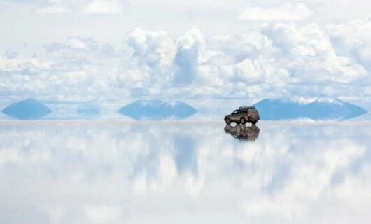 SUV sits on salt flats that reflect white cloudy sky