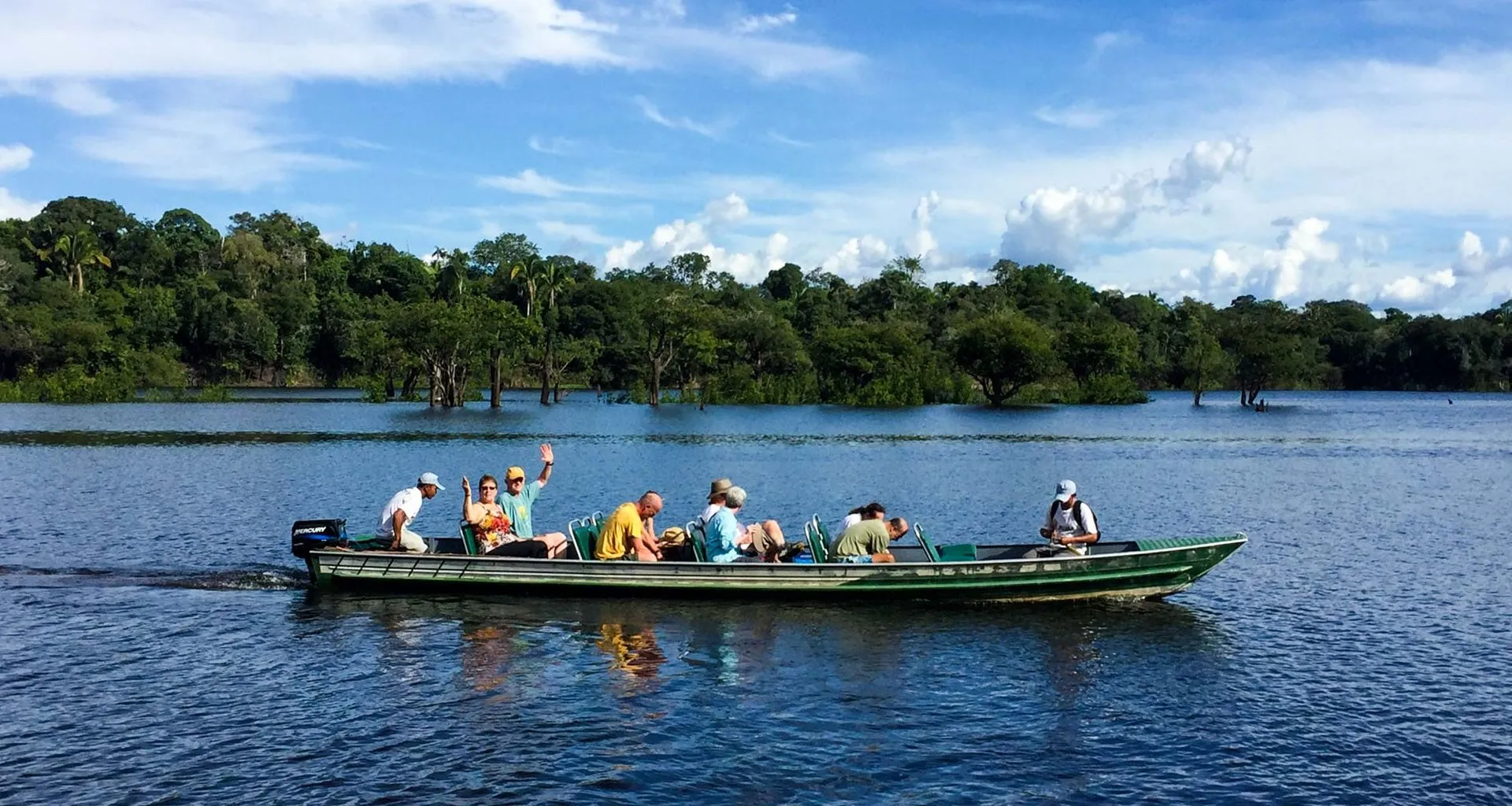 Group of travelers ride in canoe on river, some waving