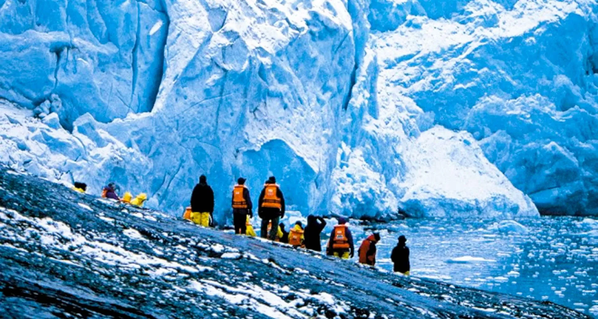 Travelers stand on rock and look up at glacier wall