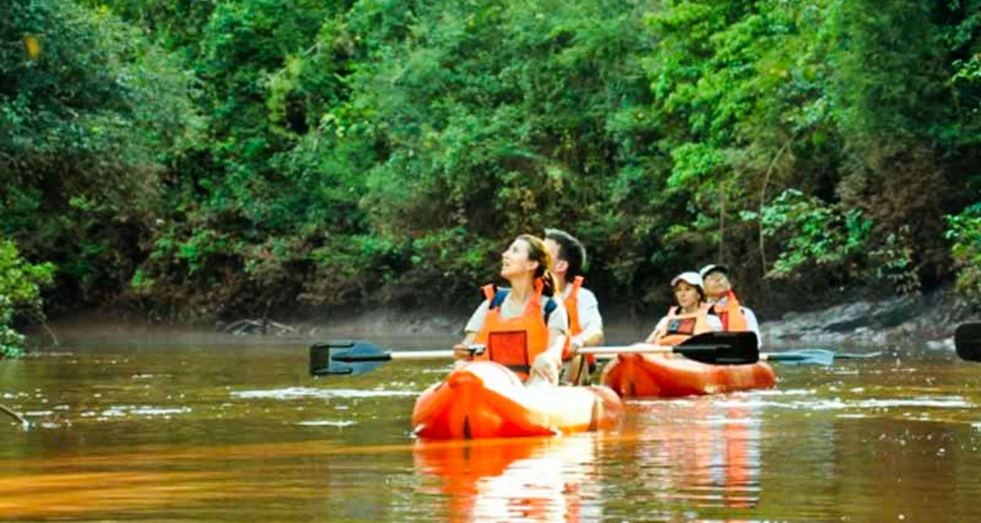 Travelers paddle orange kayaks down river