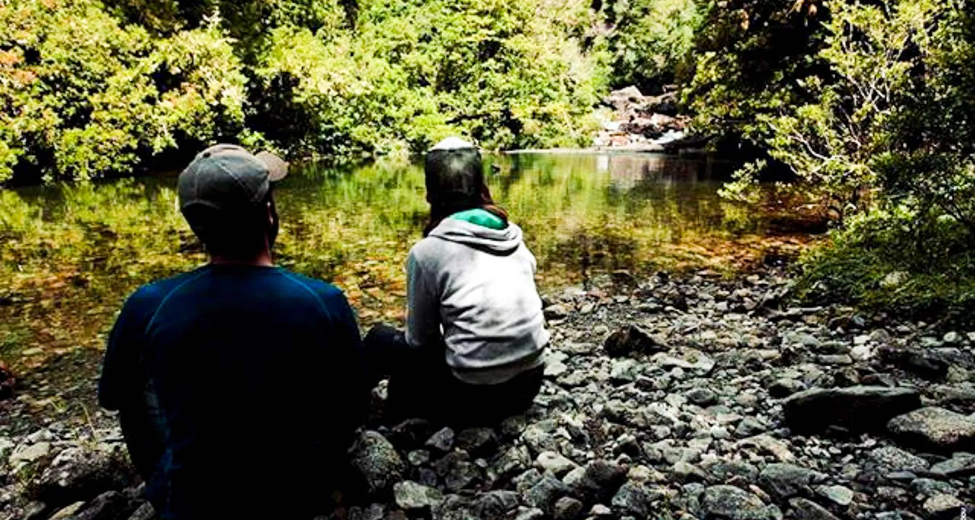 Travelers sit by forest river