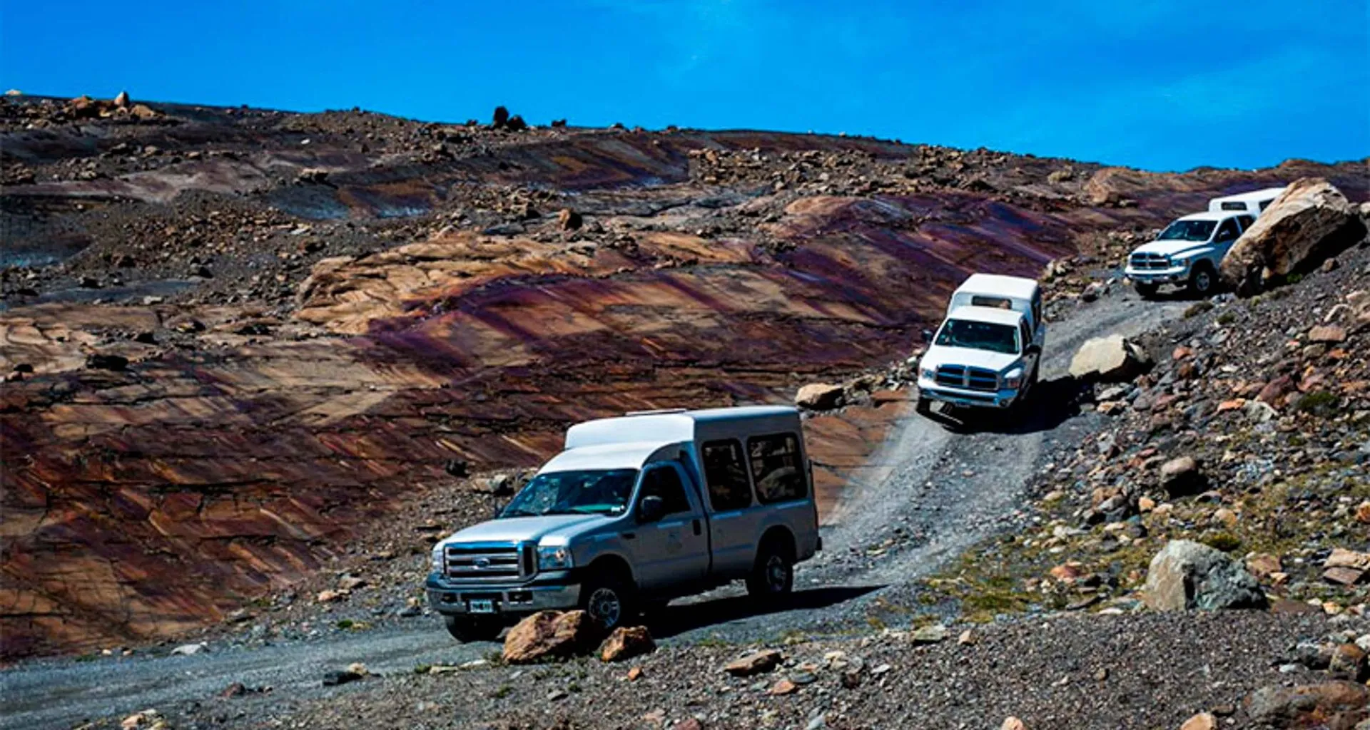 Three trucks drive down rocky desert road