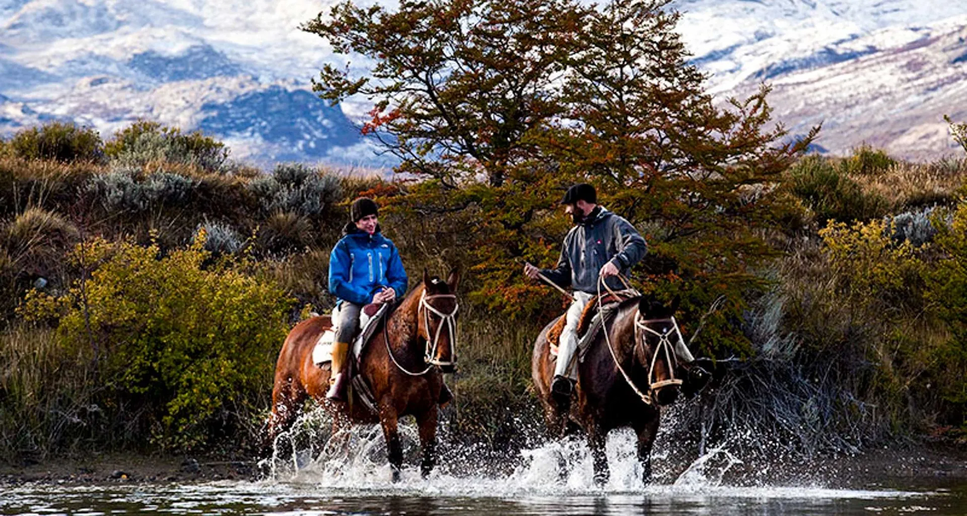 Two people ride horses through river