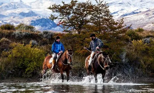 Two people ride horses through river