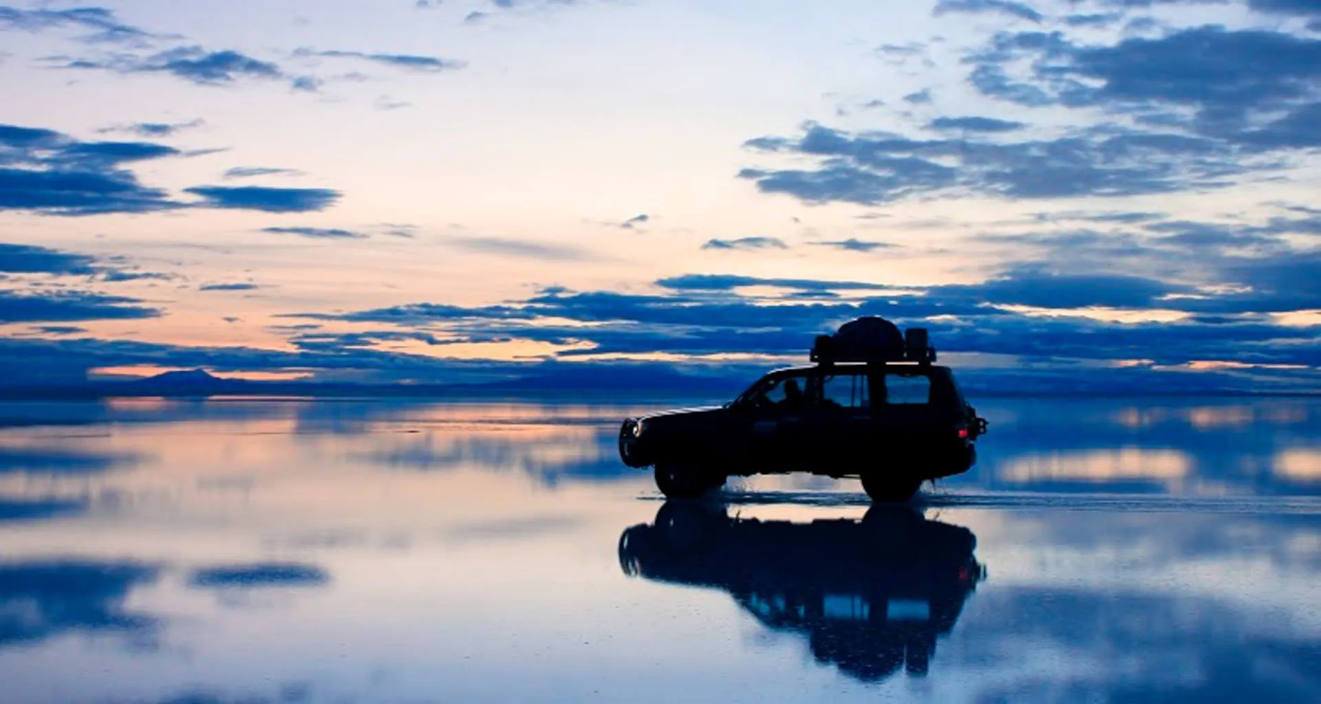 Car sits on Bolivia salt flats at evening