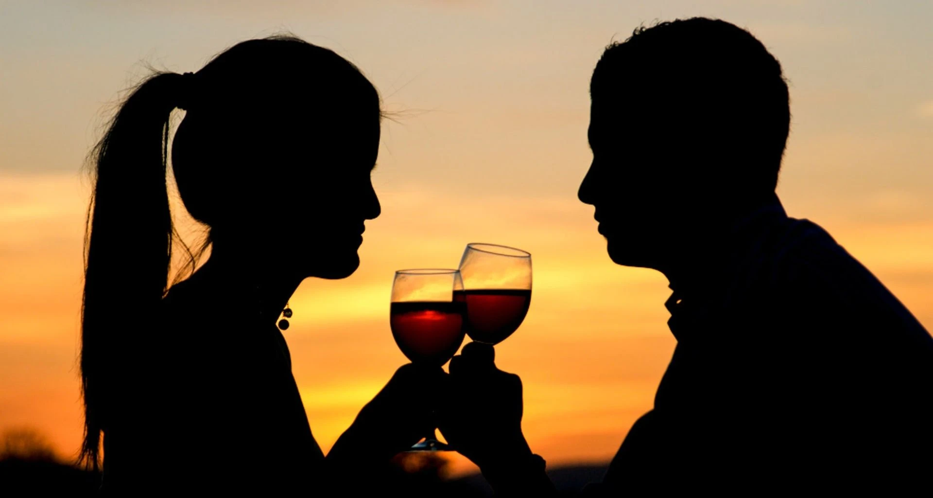 Silhouetted couple drink wine at sunset