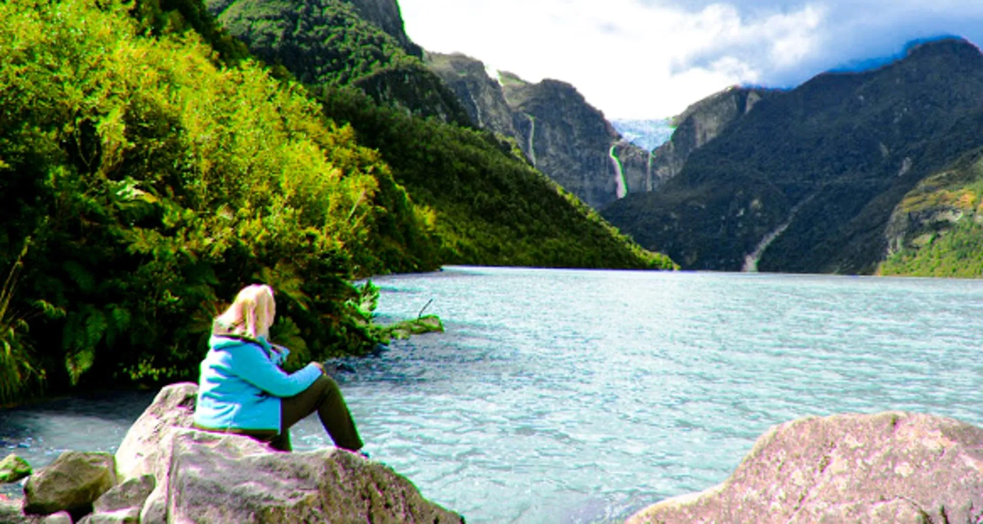 Woman sits on rock near mountain lake