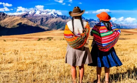 Two women din colorful shawls stand on Peru plain