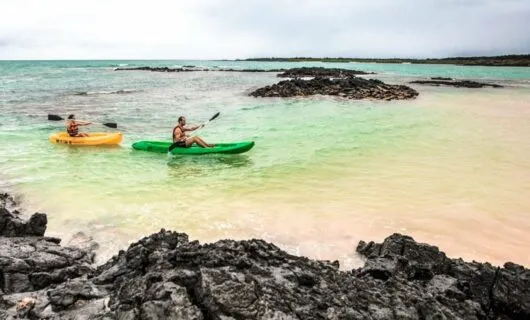 Two kayakers paddle through shallow Galapagos bay