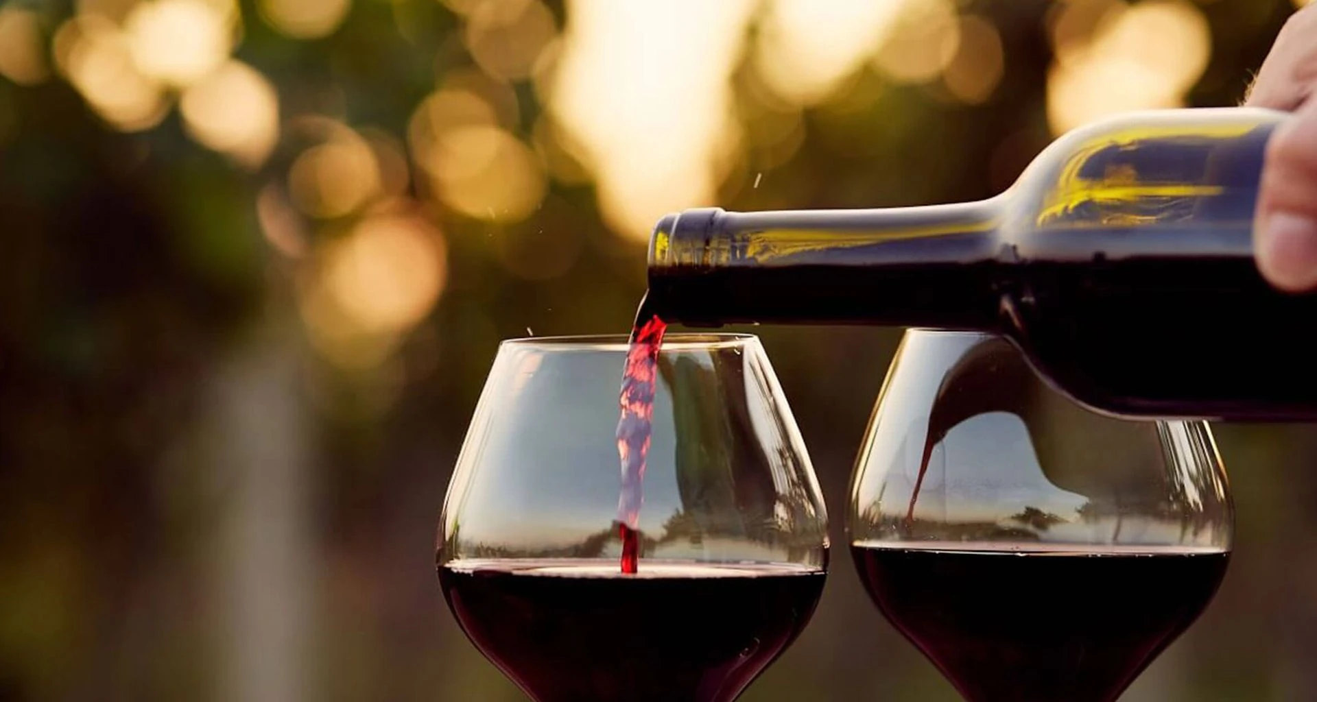 man pouring two wine glasses with red wine