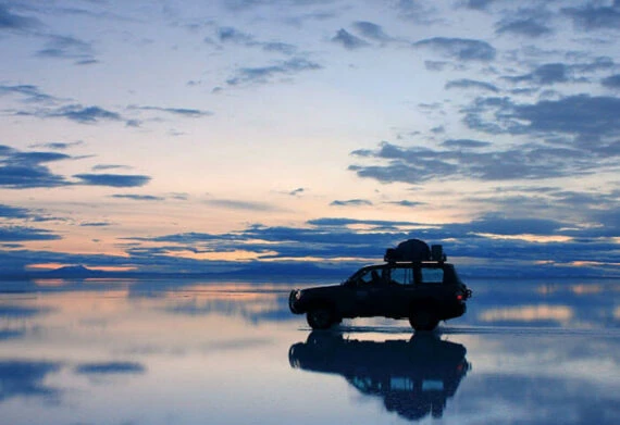 car driving through the mirrored salt flats of uyuni